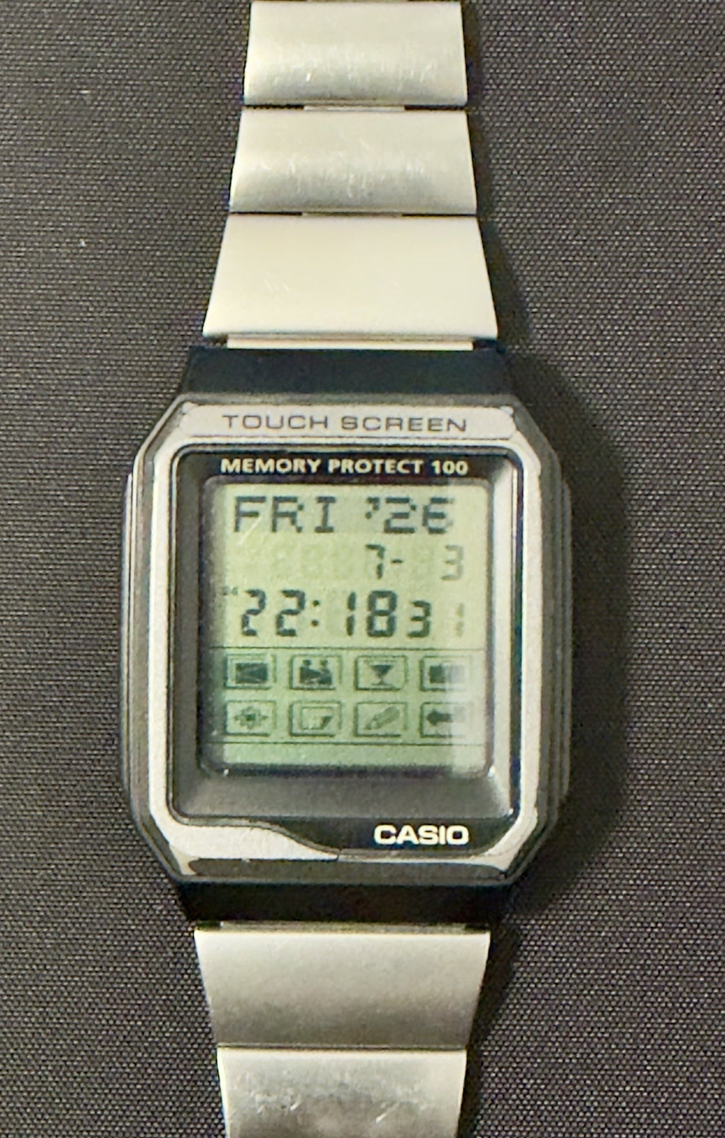 A Casio digital wristwatch with a silver metal link band, shown flat against a dark gray background.