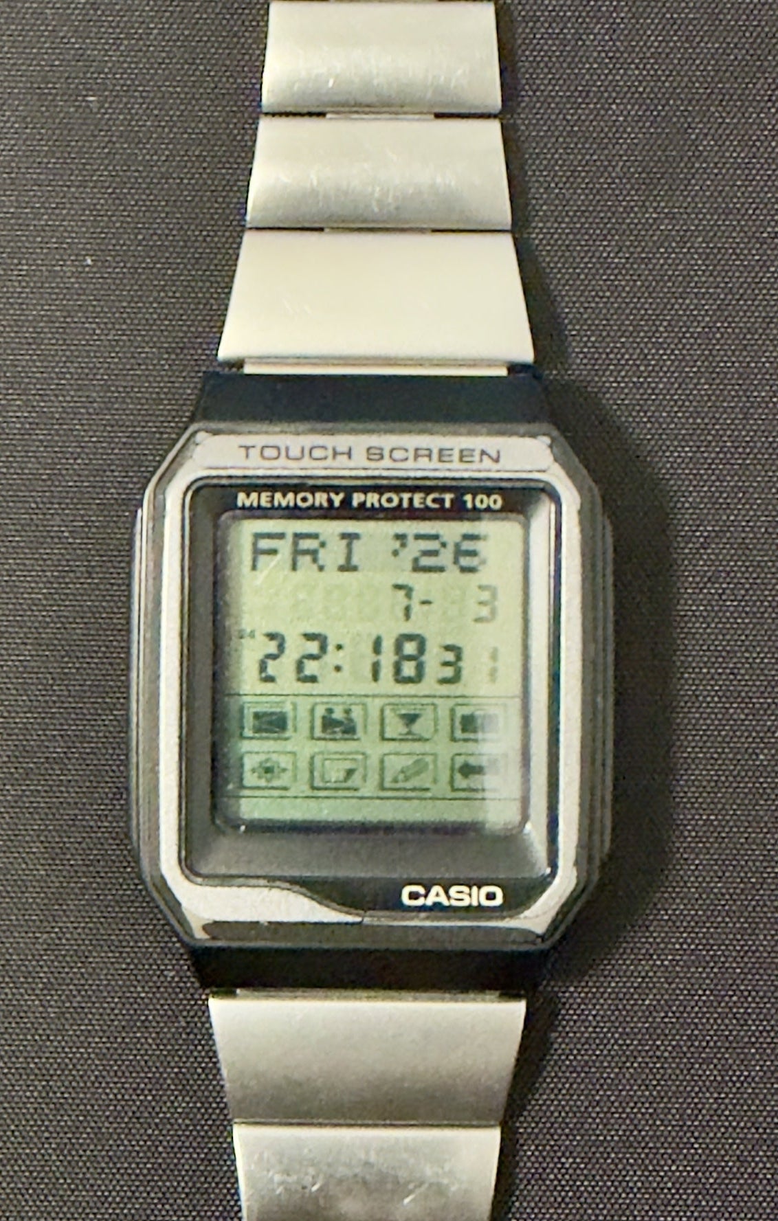 A Casio digital wristwatch with a silver metal link band, shown flat against a dark gray background.