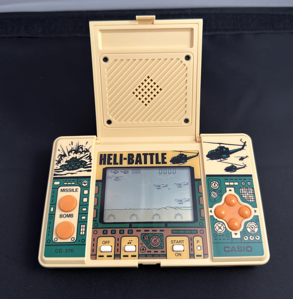 A vintage Casio handheld gaming console with a cream-colored plastic body, teal green faceplates, and orange buttons, shown with its lid open displaying the screen.