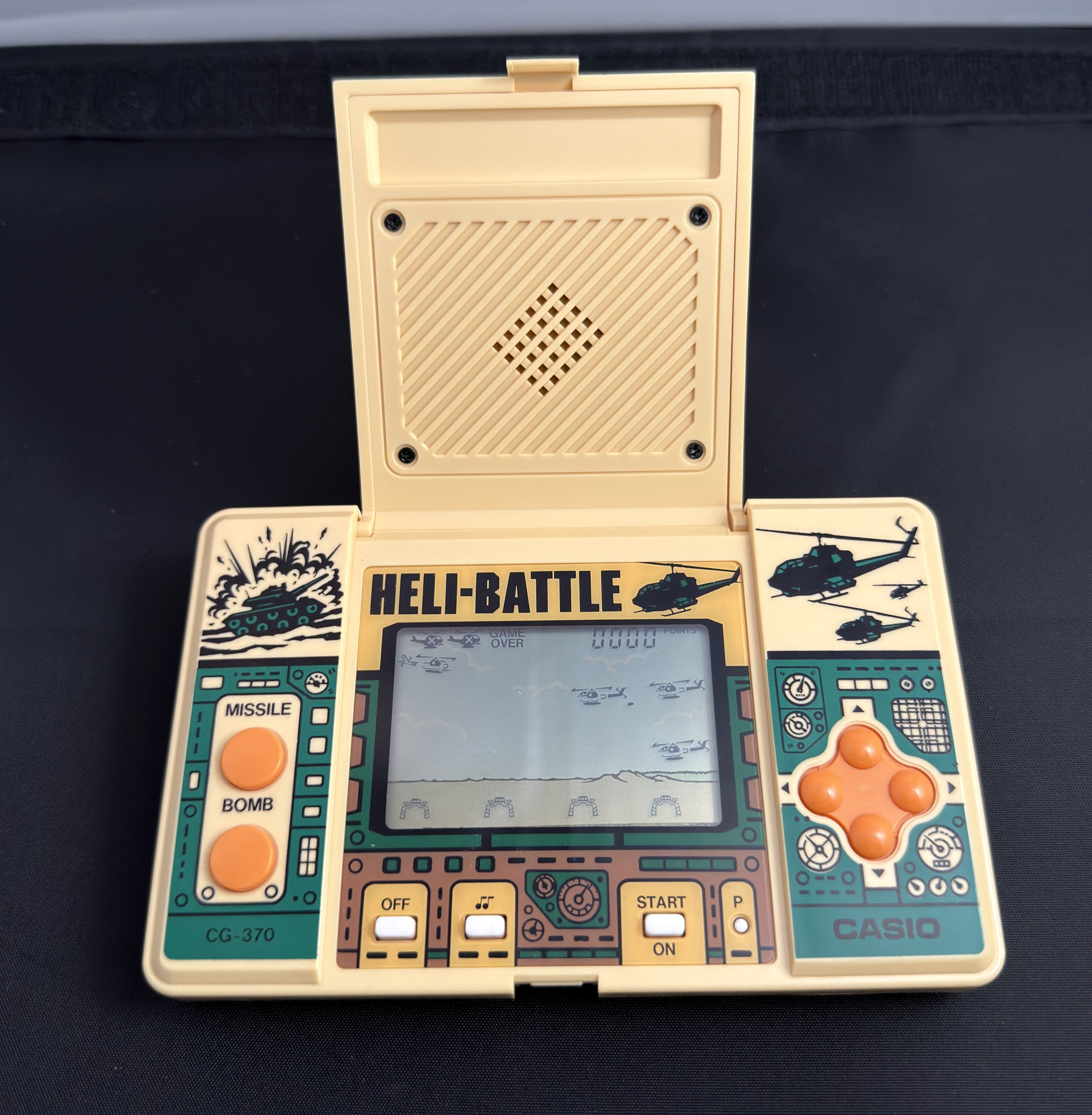 A vintage Casio handheld gaming console with a cream-colored plastic body, teal green faceplates, and orange buttons, shown with its lid open displaying the screen.