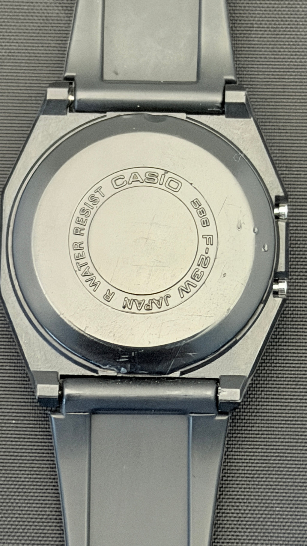 Close-up of the back of a Casio analog watch with a silver-toned metal case and dark gray strap, showing engraved text on the case back.