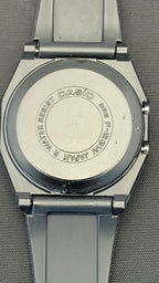 Close-up of the back of a Casio analog watch with a silver-toned metal case and dark gray strap, showing engraved text on the case back.